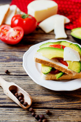 Healthy, wholesome and healthy breakfast or lunch, sandwiches with fresh avocado with spices, mozzarella cheese and tomato on a dark rustic wooden background