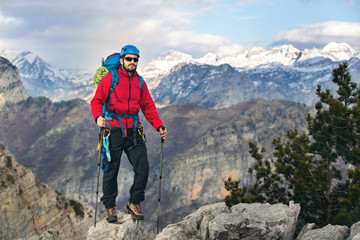 Young mountaineer standing with backpack on top of a mountain and enjoying the view