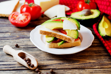 Healthy, wholesome and healthy breakfast or lunch, sandwiches with fresh avocado with spices, mozzarella cheese and tomato on a dark rustic wooden background