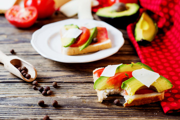 Healthy, wholesome and healthy breakfast or lunch, sandwiches with fresh avocado with spices, mozzarella cheese and tomato on a dark rustic wooden background