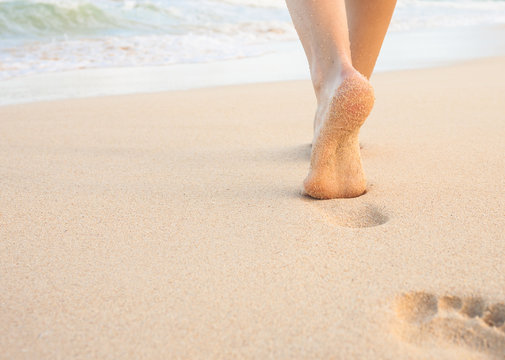 Closeup of woman's feet walking on the beach leaving footprints in the sand. 