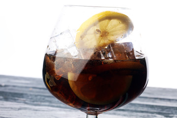 Softdrink with ice cubes, lemon and straw in glass