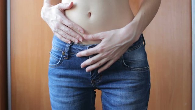 Attractive young woman in blue jeans touching her flat belly