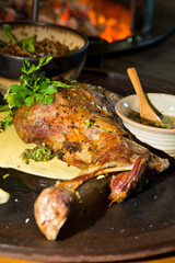 Delicious free range roasted goat shoulder served on a rustic metal plate by a hot open coal fire. Served with fresh parsley.