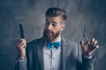 Portrait of Stylish young bearded man in a suit with bow-tie stands on a gray background and...