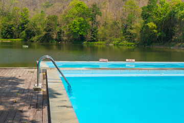 Blue swimming pool with wooden flooring near the lake mountain and tree with blue sky