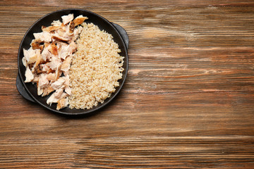 Frying pan with delicious chicken and rice on wooden table