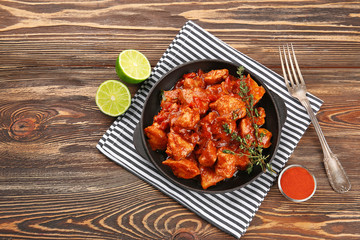 Frying pan with delicious chicken tikka masala on wooden table