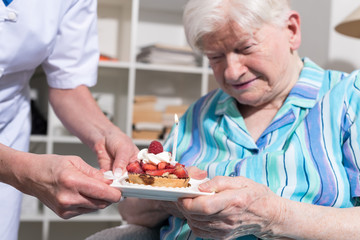 Senior woman receiving a little birthday cake from her nurse