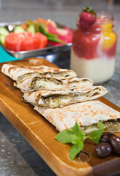 Lebanese manakeesh manouche with zaatar, served on a rustic wooden board with mint leaves, olives and a strawberry smoothie.