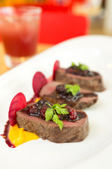 Organic Venison served with fresh raspberry raspberry sauce, beetroot slices and pumpkin puree, on a white plate.