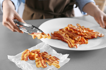 Woman holding tasty bacon slice with tongs