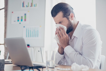 Sick businessman with temperature works in office and wipes his nose with a napkin
