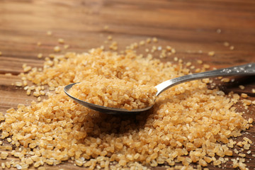 Heap of brown sugar and spoon on wooden background