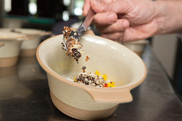 Organic quinoa grain being placed into a rustic ceramic bowl