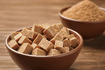 Brown sugar cubes in bowl on wooden background