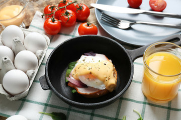 Frying pan with tasty egg Benedict on table