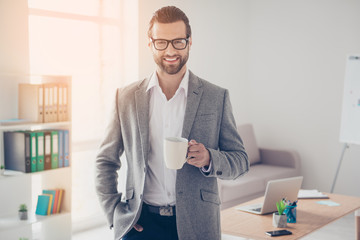 Happy handsome businessman in white shirt and jacket holds mug of drink in office while taking hand...