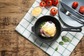 Frying pan with tasty egg Benedict on table