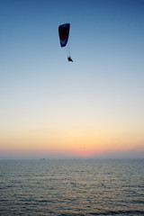 Powered paraglider flying over the sea at sunset sky background