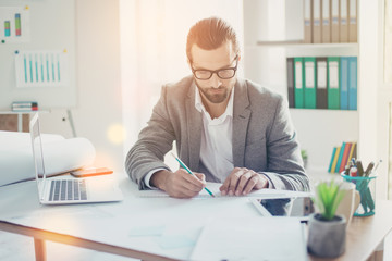 Stylish handsome concentrated man  in formal wear has ideas and working with blueprint papers and drawings in modern lightful office