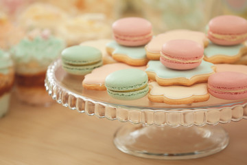 Glass stand with tasty macarons and cookies on table, closeup