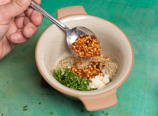 A bowl of chilli flakes, fresh parsley, garlic and oregano being prepared for mixing.
