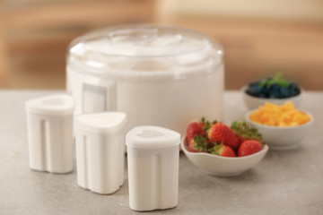 Cups, yogurt maker and ingredients on kitchen table