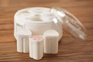 Cups and modern yogurt maker on wooden table