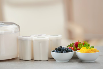 Modern yogurt maker, cups and ingredients on kitchen table