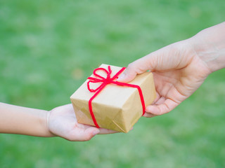 holidays, present, christmas, childhood and happiness concept - close up of child and mother hands with gift box over green background