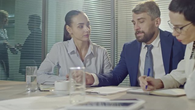 PAN of bearded businessman looking at document and making suggestions and remarks to businesswomen making notes 