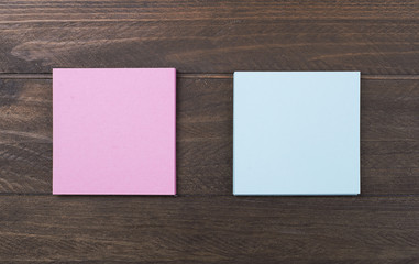 Pink and blue paper note on wooden background.