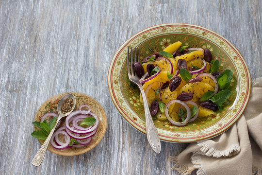 Moroccan salad of oranges with red onions, olives and zira on a wooden table