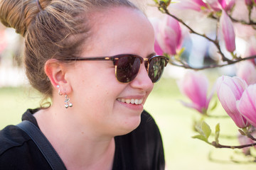 Junge Frau mit Sonnenbrille unter Magnolienblüten, Lachend - obrazy, fototapety, plakaty