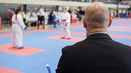 Martial art competitions - bald man coach-judge looking at karate teenager's fighting