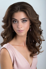 Portrait of a brunette with voluminous curls and a gentle make-up in a light pink dress.