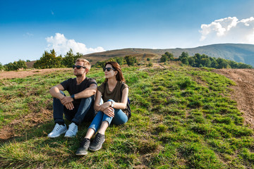 Young couple smiling, enjoying mountains lanscape, sitting on hill.