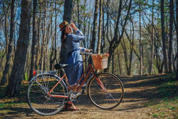 Fototapeta na wymiar Beautiful young smiling woman with short dark hair and hat standing near bicycle with basket of huge bouquet of chamomiles.Summer girl enjoying the nature outdoor.Green background.