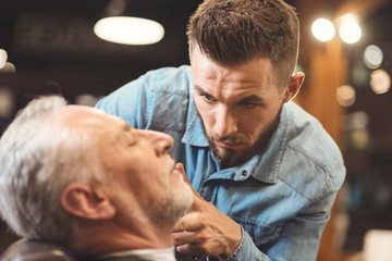 Peaceful barber styling beard of the old man in barbershop