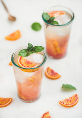 Blood orange fresh summer homemade lemonade with ice and mint in glasses, light grey marble background, selective focus