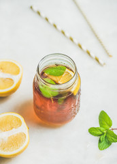 Summer cold Iced tea with fresh bergamot, mint and lemon in glass jar on light table background