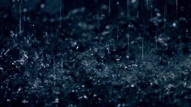 Rain drops hitting puddle in the dark close-up slow motion shot