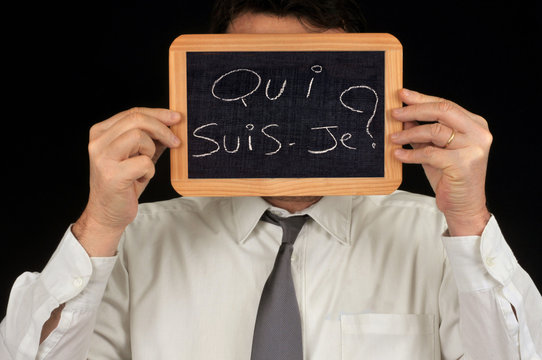 Homme tenant une ardoise lui cachant le visage avec qui suis-je &eacute;crit dessus 