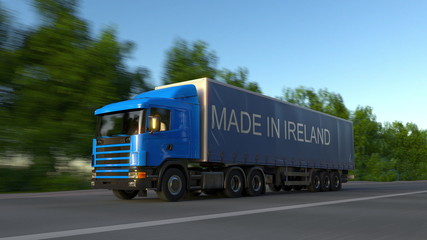 Fototapeta na wymiar Speeding freight semi truck with MADE IN IRELAND caption on the trailer. Road cargo transportation. 3D rendering