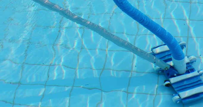 Worker cleans his swimming pool with long brush and automatic pool cleaner.