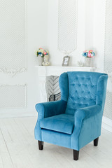 Interior of a snow-white living room with a blue vintage armchair and fireplace