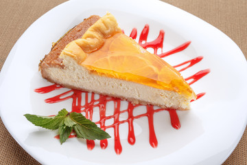 Orange cheesecake served on a white plate with mint and strawberry sauce