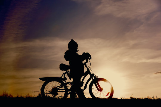 little boy riding bike at sunset sky