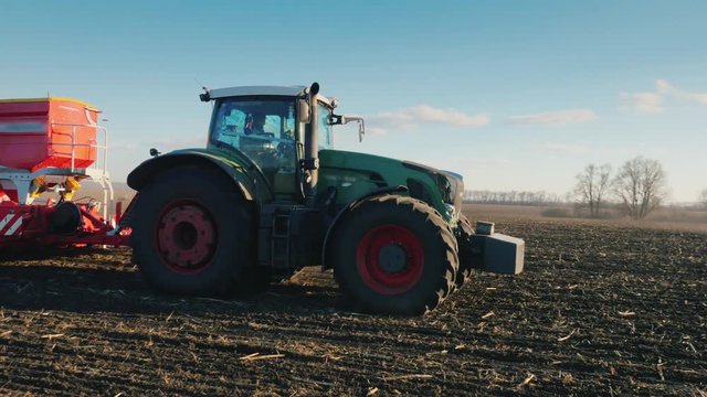 Steadicam pan shot: A tractor with a large seeder is driving across the field in the sun.
